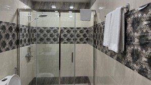 A modern bathroom with a glass-enclosed shower, marble walls, and a toilet.