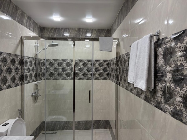 A modern bathroom with a glass-enclosed shower, marble walls, and a toilet. - Central City Department Hotel (Baku)
