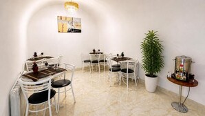 A dining area with white chairs, a chandelier, a potted plant, and a small table with a pot.