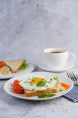 Un plato con un sándwich, una taza de café y un tenedor sobre una mesa.