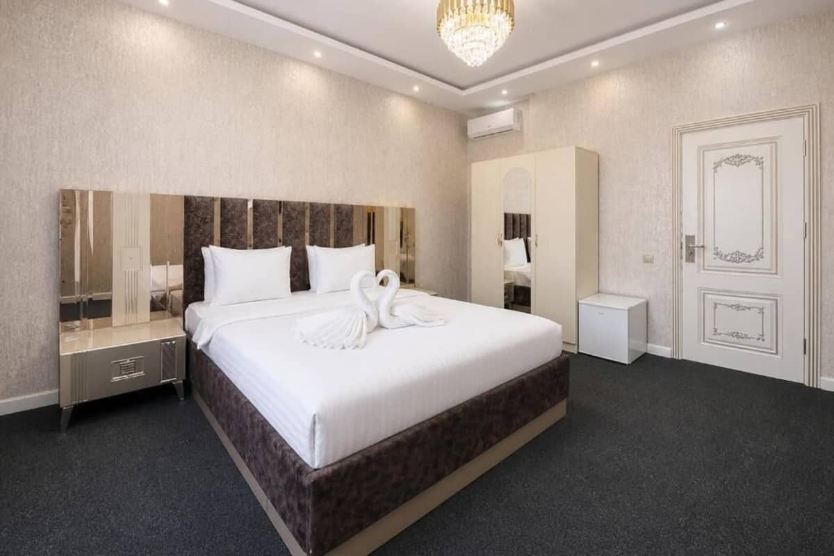 A hotel room with a large bed, a chandelier, a mirror, and a door with decorative moldings.
