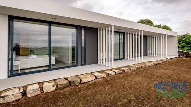 Ein modernes Haus mit großen Glasüren, die in ein Schlafzimmer mit Bett und Sessel führen.