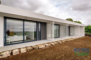 Ein modernes Haus mit großen Glasüren, die in ein Schlafzimmer mit Bett und Sessel führen.