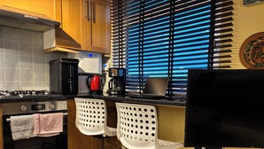 Eine Küche mit Herd, Backofen, Kaffeemaschine und zwei weißen Stühlen mit Lochmuster.