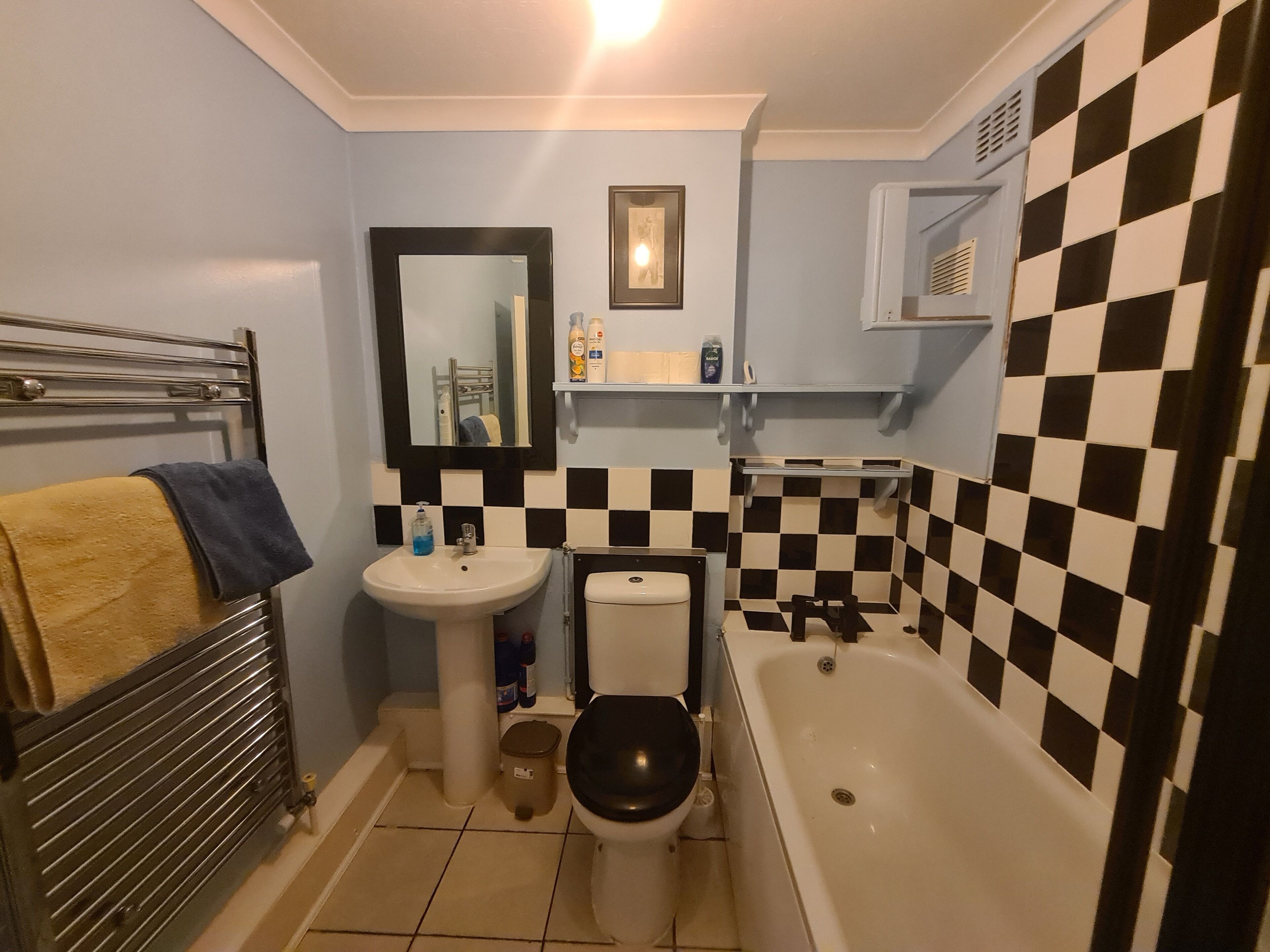 A bathroom with a toilet, sink, and bathtub. There is a towel rack with a yellow towel and a blue towel. A mirror hangs on the wall above the sink.