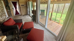 Un cuarto acogedor con pared de piedra, techo de madera y amplios ventanales correderos que dan a una terraza exterior.