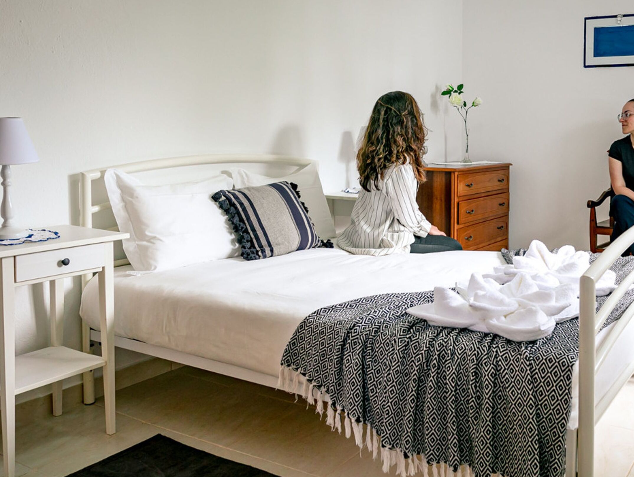 A neatly made bed with a patterned blanket, a bedside table with a lamp, and a dresser.