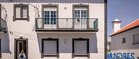 Un edificio de dos pisos con un balcón, una puerta y un letrero en la pared.