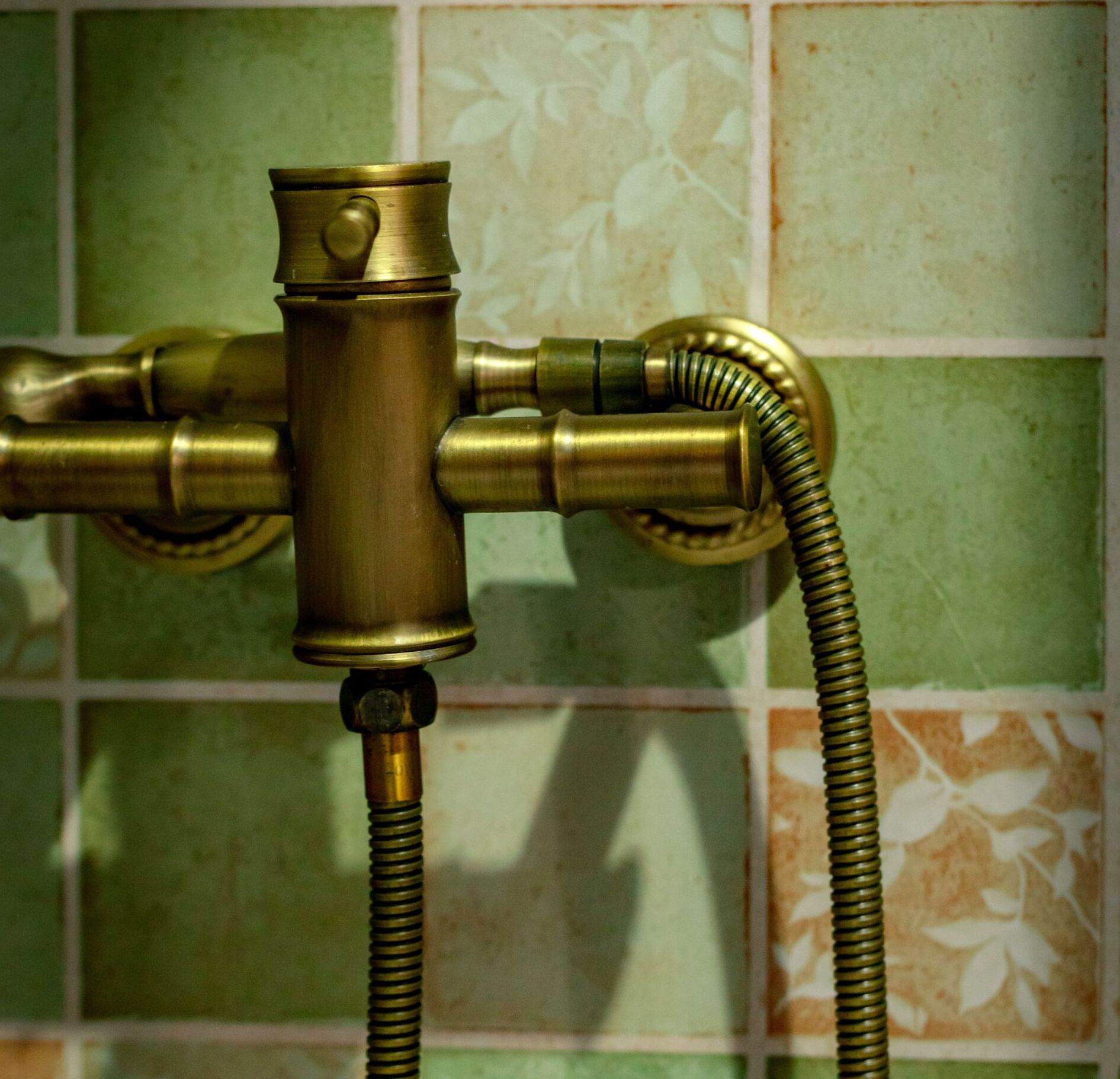 Un cabezal de ducha de latón con una manguera flexible unida, montado en una pared de azulejos con un estampado floral.