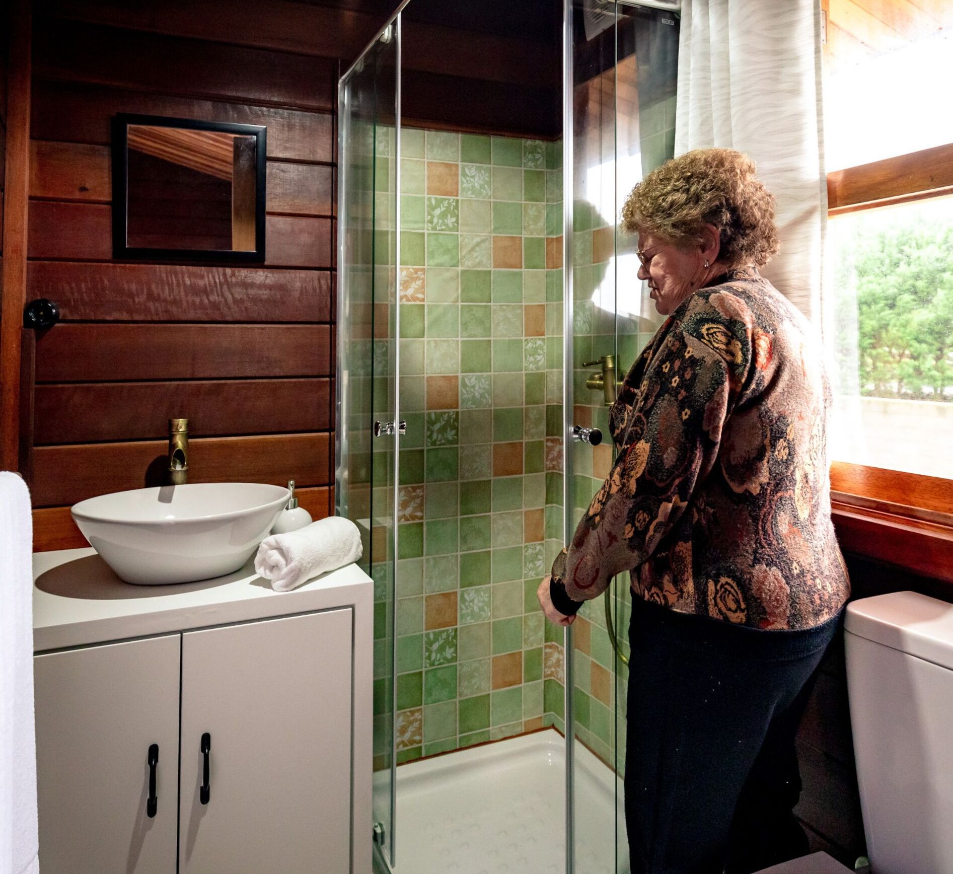 A bathroom with a white sink, a glass shower enclosure, and wooden walls.