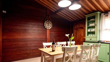 A wooden interior with a dining table set for two, a clock on the wall, and a green cabinet with dishes.