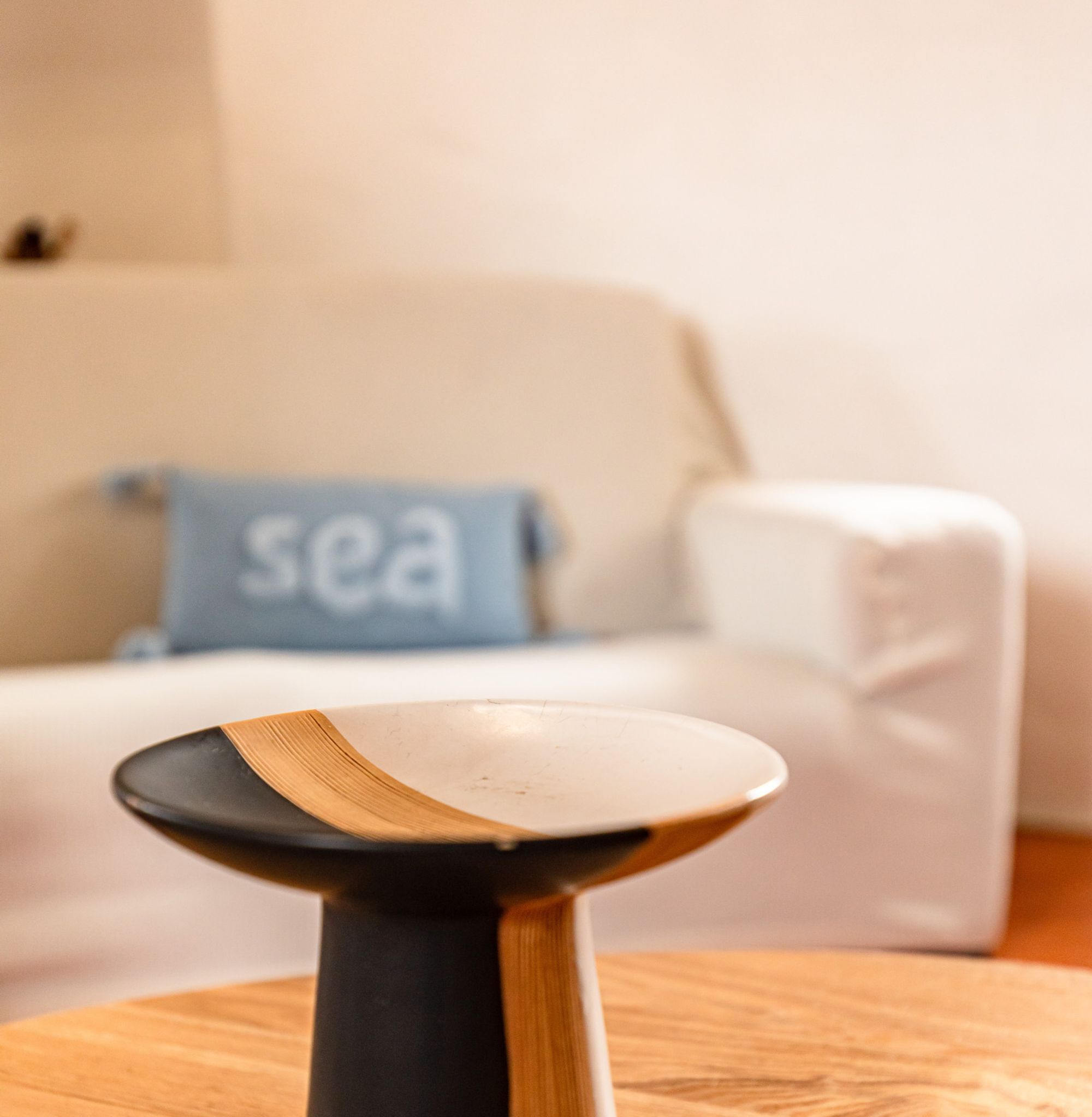 Un tavolo di legno con un piatto bianco in una stanza con un divano bianco e un cuscino blu con la scritta 'sea'.