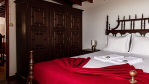 A neatly made bed with a red blanket, a wooden headboard, and a nightstand with a lamp. - Moinho Pedra Pomes in Santa Cruz da Graciosa (Santa Cruz da Graciosa)