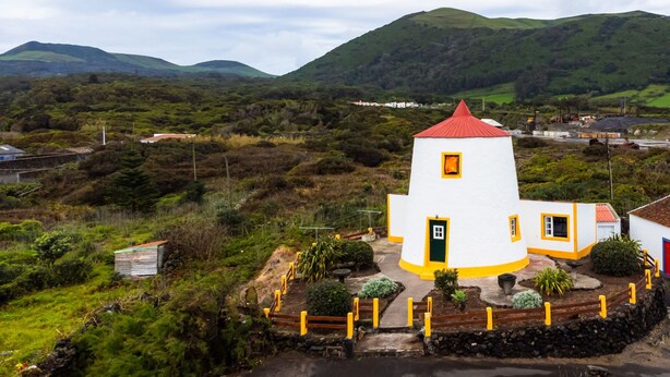 A white building with a red roof, surrounded by greenery and hills. - Moinho Pedra Pomes in Santa Cruz da Graciosa (Santa Cruz da Graciosa)