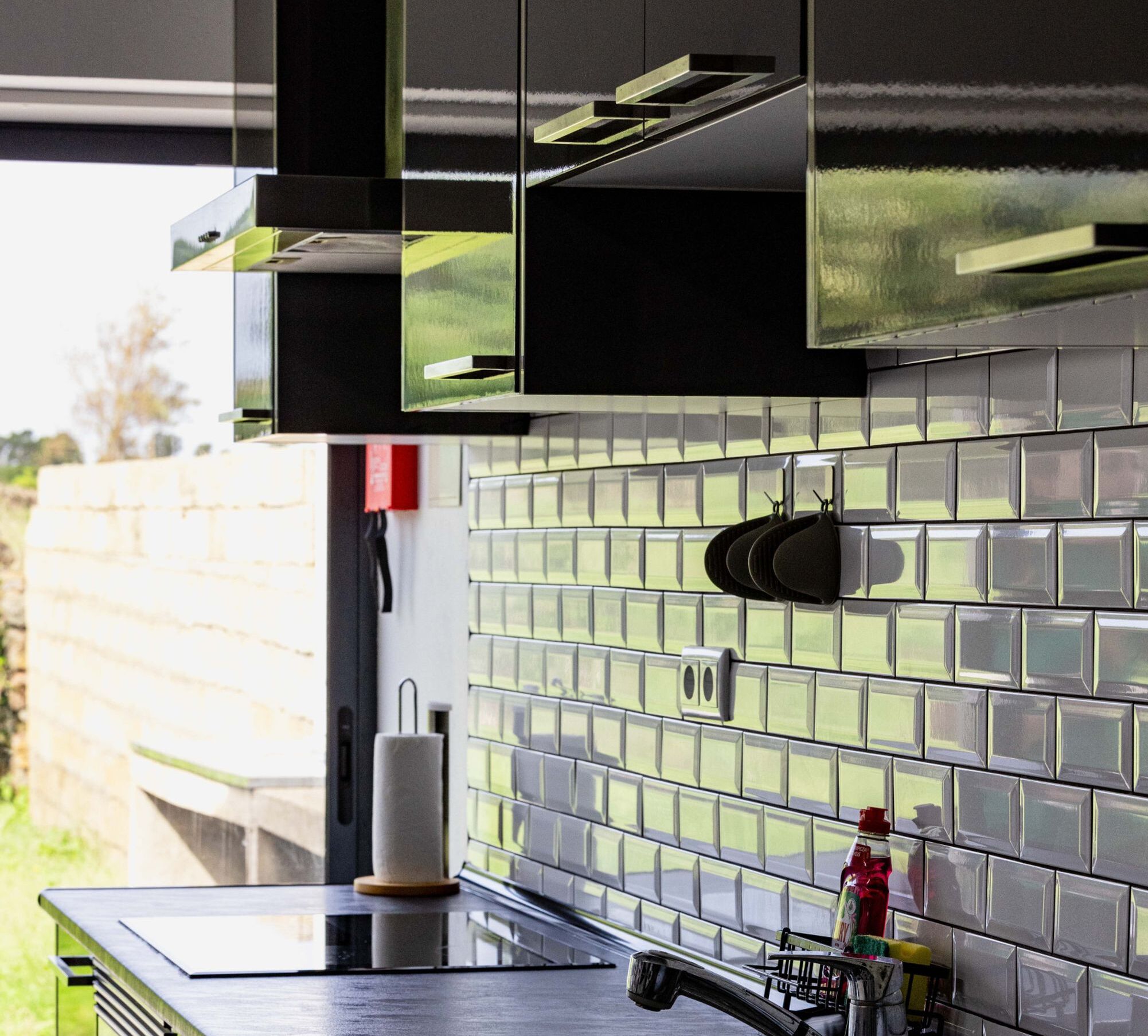 A modern kitchen with black cabinetry, a tiled backsplash, and a stainless steel countertop.