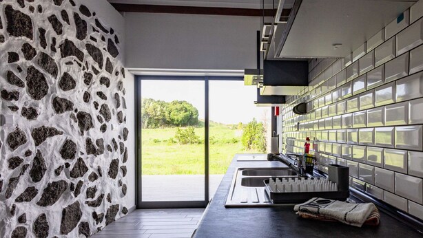 Une cuisine moderne avec un mur en pierre, une grande fenêtre et un pare-feu en carreaux.