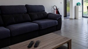 Un salon moderne avec un canapé gris foncé, une table basse en bois sur laquelle reposent deux télécommandes, et un extincteur fixé au mur.