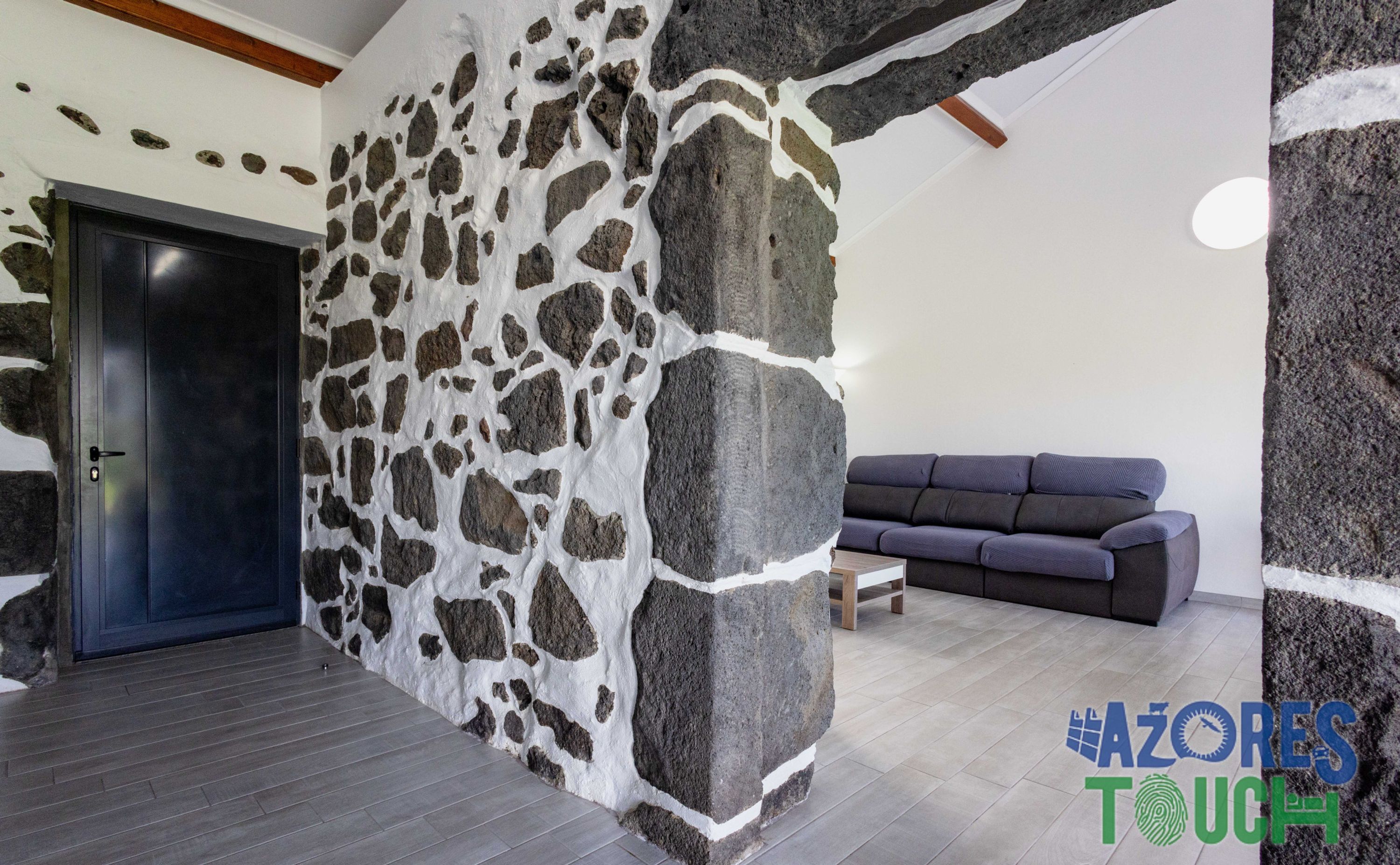 A room with a stone wall, a dark door, a gray sofa, and a wooden coffee table.
