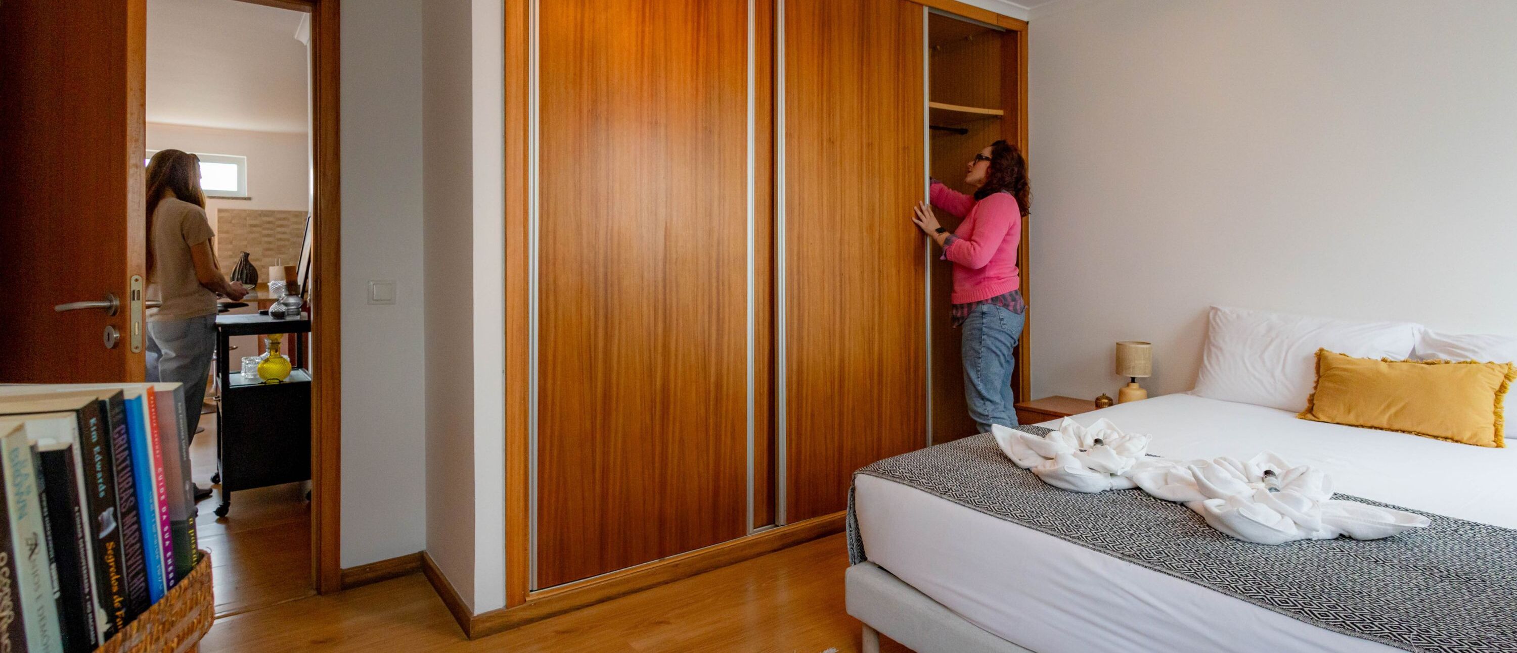 Una habitación de hotel con una cama, un armario de madera, una mesita de noche con lámpara y otra mesita de noche con lámpara.