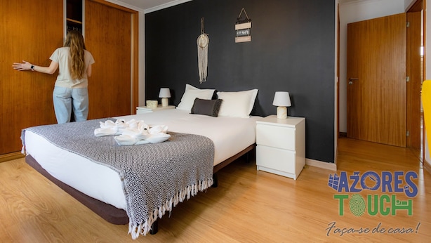 A bedroom with a bed, bedside tables, a wardrobe, and a wall-mounted macrame piece. - Olis House in Angra do Hero smo (Angra do Heroismo)