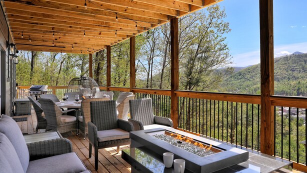Una terraza techada al aire libre con mobiliario de mimbre, una chimenea y vistas a un paisaje montañoso.