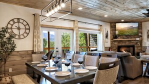 Un comedor con una gran mesa dispuesta para seis comensales, una chimenea y una vista panorámica a través de las ventanas.