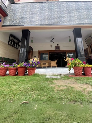 A building with a covered entrance, a ceiling fan, and potted plants in front. - Samar Niwas Dehradun (Dehradun)