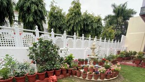 Un jardín bien cuidado con una fuente central, rodeado de plantas en macetas y una valla blanca.