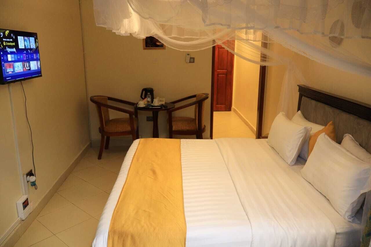 A hotel room with a bed, a TV mounted on the wall, a small table with chairs, and a door leading to another room.