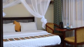 A hotel room with a bed, a chair, a small table, and a hanging light fixture. - Hotel Casabella (Entebbe)