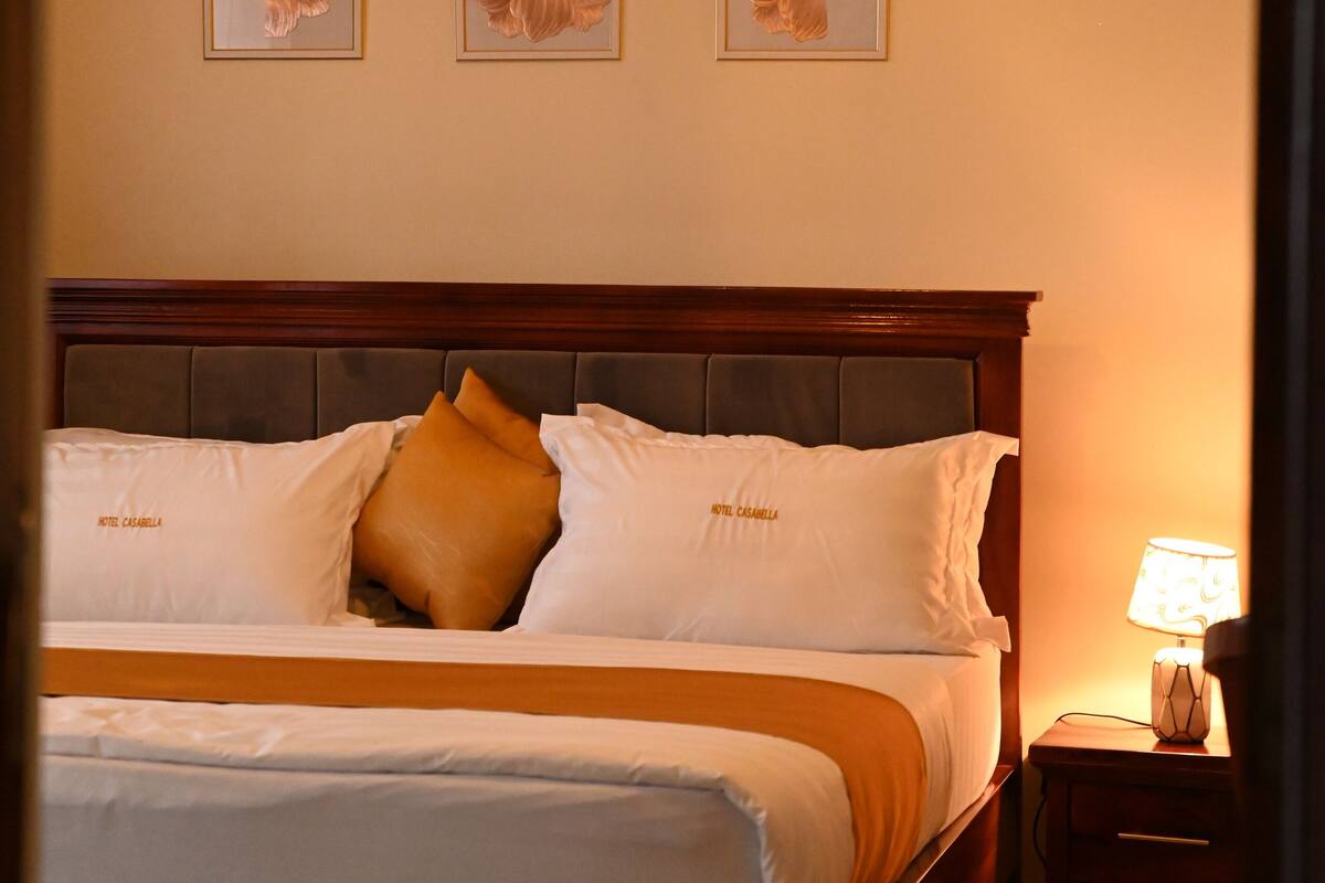 A neatly made bed with a wooden headboard, a bedside lamp, and framed artwork on the wall.