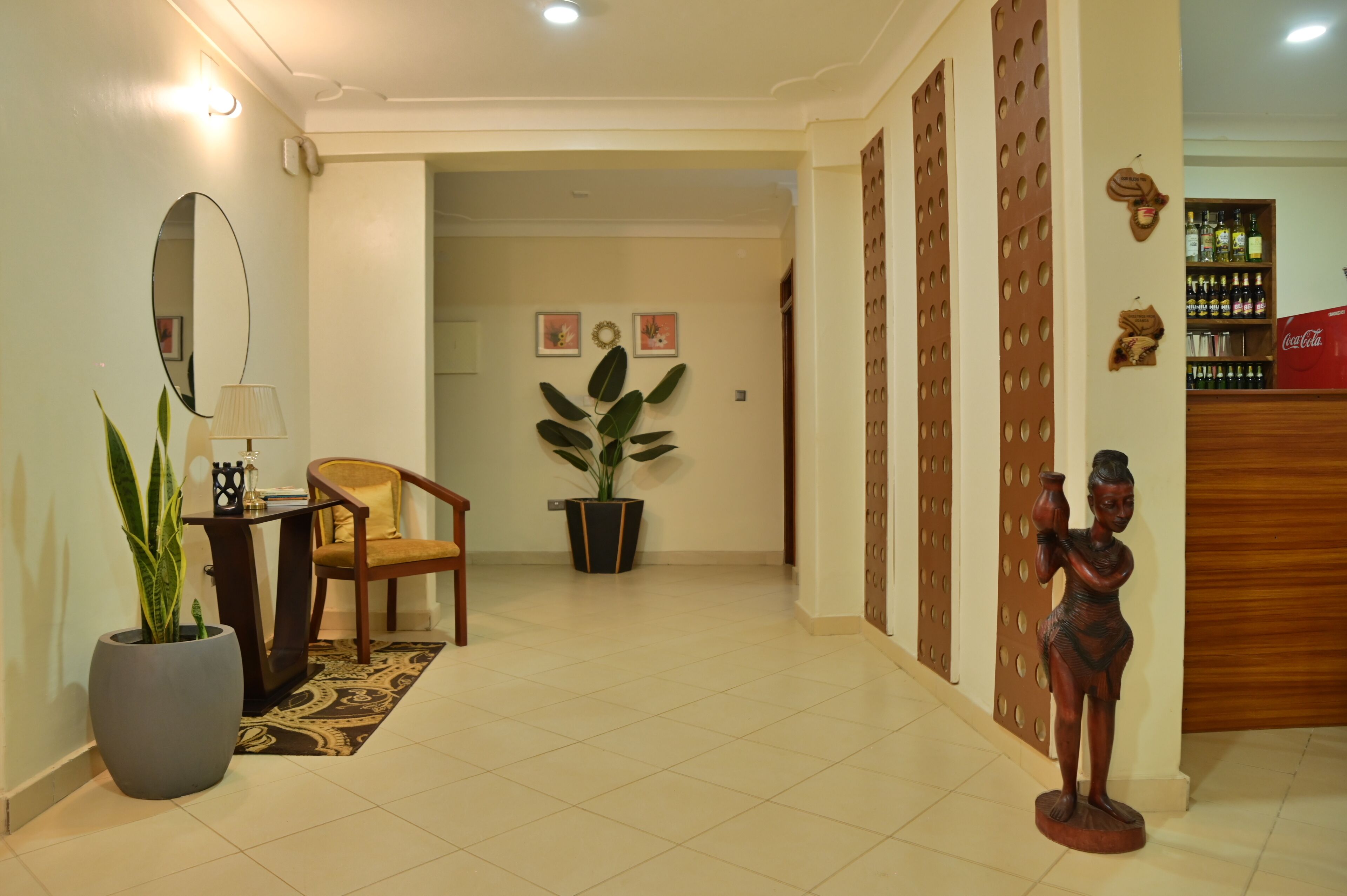 A hallway with a potted plant, a chair, a table with a lamp, a mirror, and a statue.
