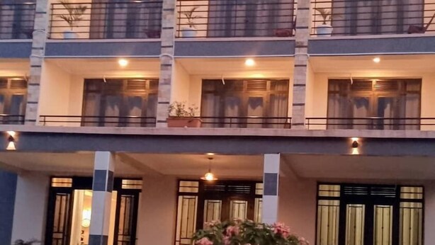 A multi-story hotel with balconies, a central courtyard with a circular seating area, and a well-maintained garden. - Hotel Casabella (Entebbe)