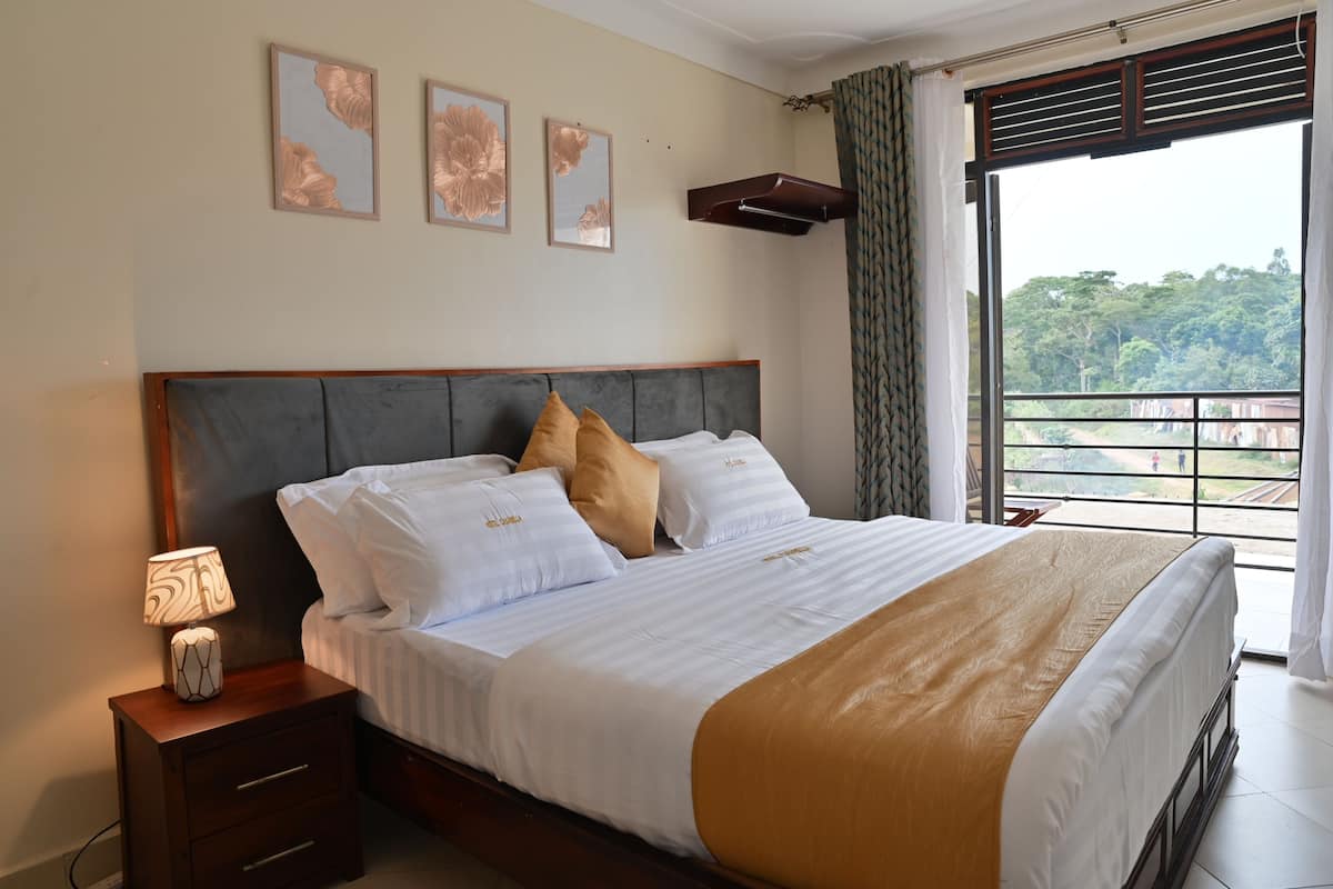 A neatly made bed with white and gold bedding, a bedside lamp, and a nightstand. There are three framed floral artworks on the wall above the bed.