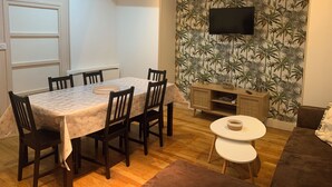 A dining area with a table and chairs, a small white table, a sofa, and a wall-mounted TV. - Gite La motte Forte, Arnay le Duc (Arnay-le-Duc)