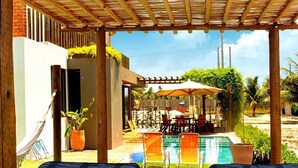 Un espacio al aire libre cubierto con piscina, sillas de descanso y una zona de comedor con sombrillas.