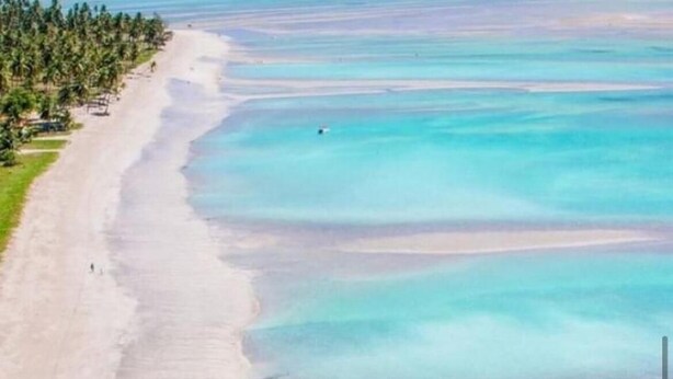 Vista aérea de una playa con aguas turquesas cristalinas, una orilla arenosa y un bote anclado cerca de la orilla.