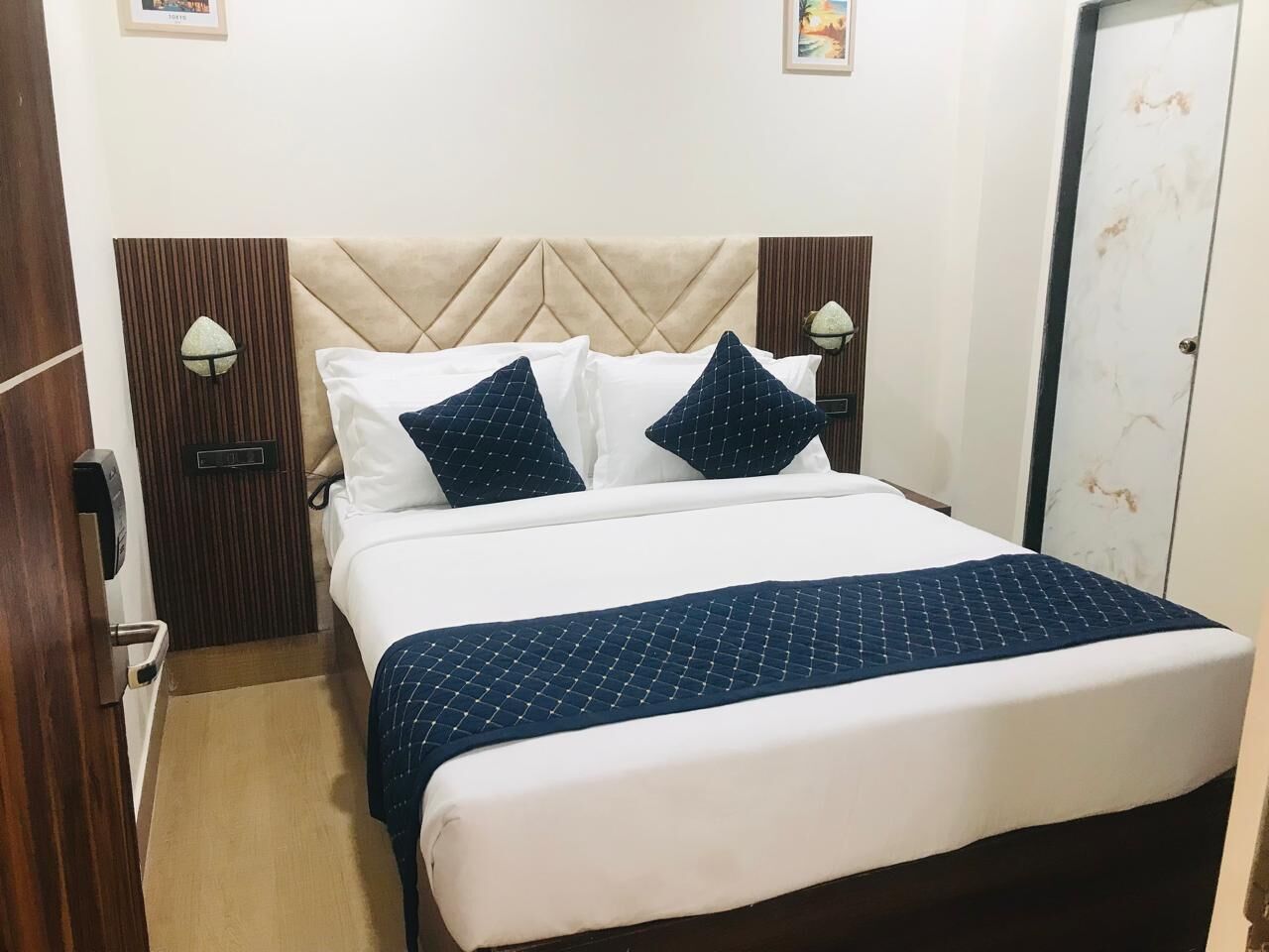 Una cama bien hecha con colcha blanca y azul marino, dos almohadas azul marino y un cabecero de madera.