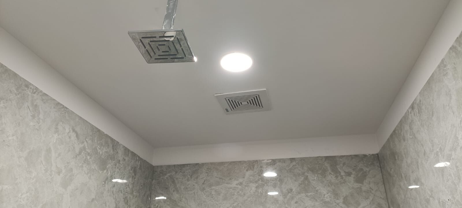 Un soffitto con illuminazione a incasso e due bocchette quadrate.