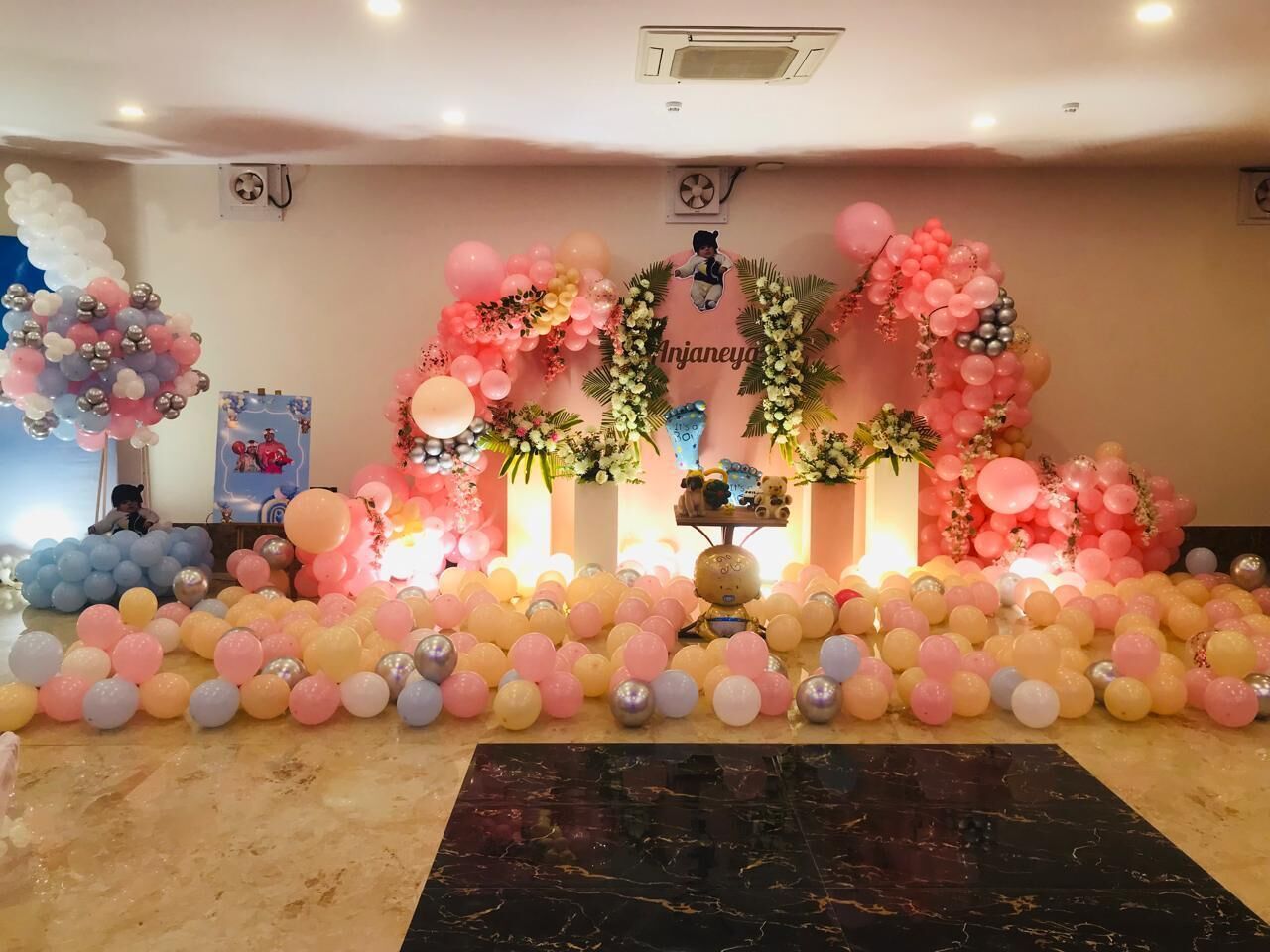 A decorated event space with a stage, balloons, and floral arrangements.
