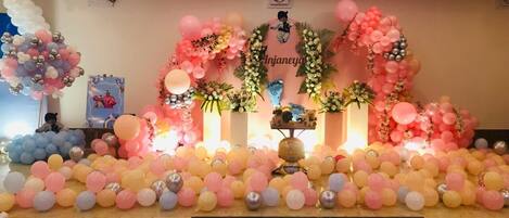A decorated event space with a stage, balloons, and floral arrangements.