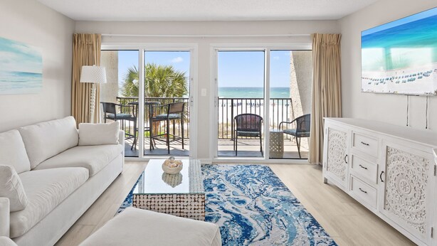 A modern hotel room with a white sofa, a coffee table, a patterned rug, a white cabinet, and a balcony with a view of the beach. - Windancer 209. Gulf Front Condo, Free Beach Service, Pool, Grill, Sugar Sand! (Miramar Beach)
