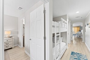 A modern hotel room with a bunk bed, a bedside table with a lamp, and a view of the hallway.