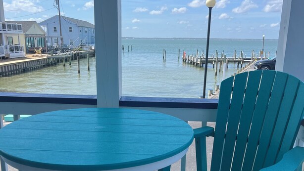 A teal chair and table on a wooden deck with a view of a dock and water. - 1st Floor Direct Bayfront 1 bedroom Updated Condo with pool overlooking the bay! (Ocean City)