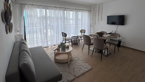 Una sala de estar moderna con un sofá, una mesa de comedor, sillas y un televisor montado en la pared.
