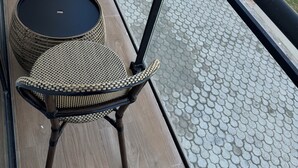 Un balcón con mobiliario de mimbre, una piscina y suelo de baldosas.