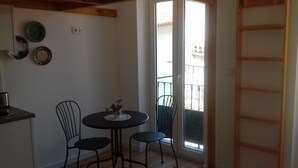 Ein kleiner Essbereich mit einem runden Tisch und zwei Stühlen, einer kleinen Vase mit Blumen und Blick auf einen Balkon durch eine Glastür.