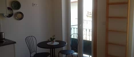 A small dining area with a round table and two chairs, a small vase with flowers, and a view of a balcony through a glass door.