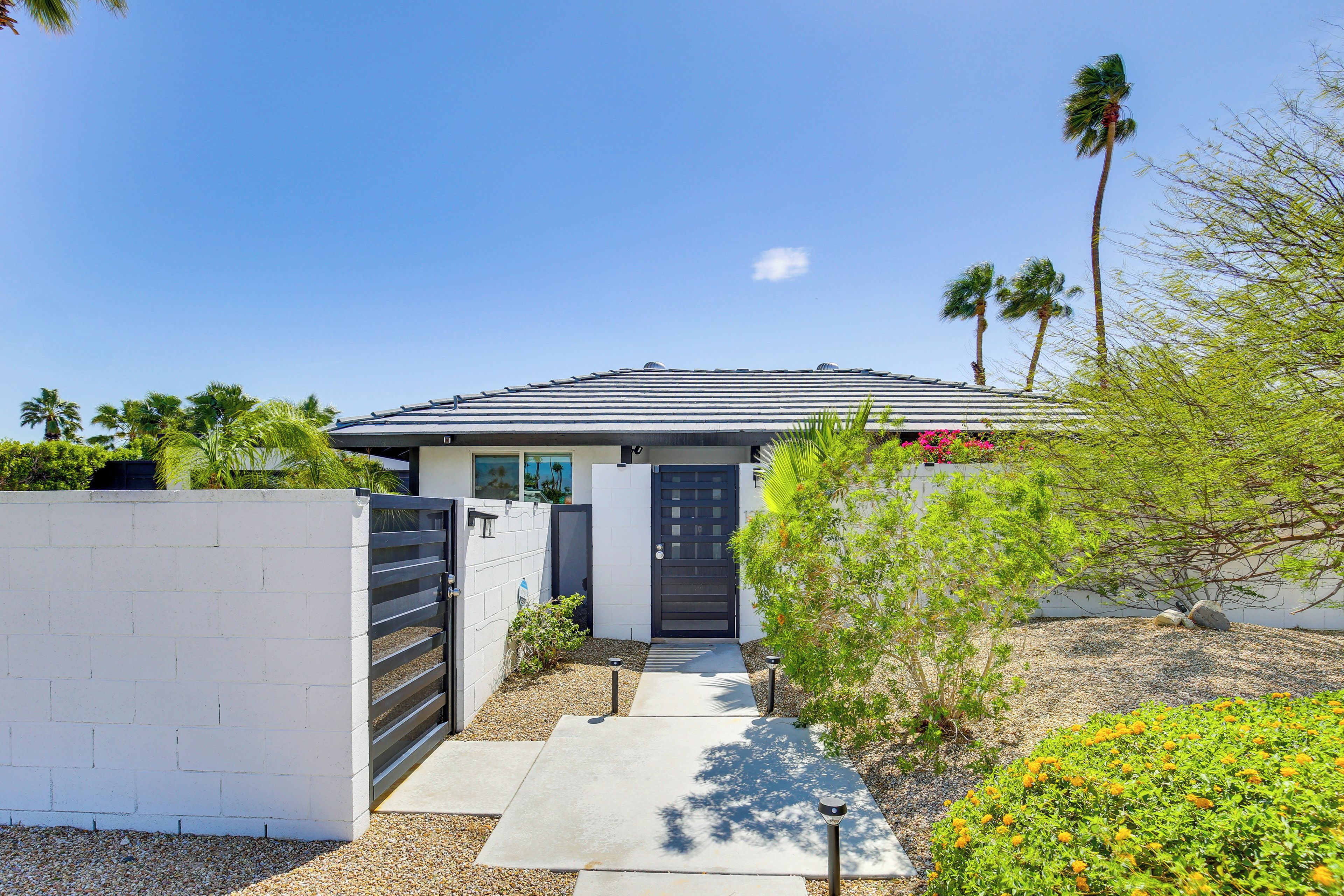 A modern house with a gated entrance, a concrete pathway, and a well-maintained garden with orange flowers.