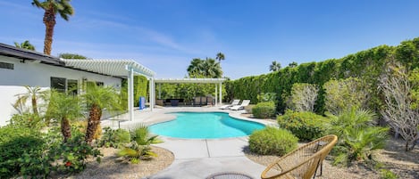 Un área de piscina moderna al aire libre con una pérgola, sillas de descanso y un jardín bien cuidado.